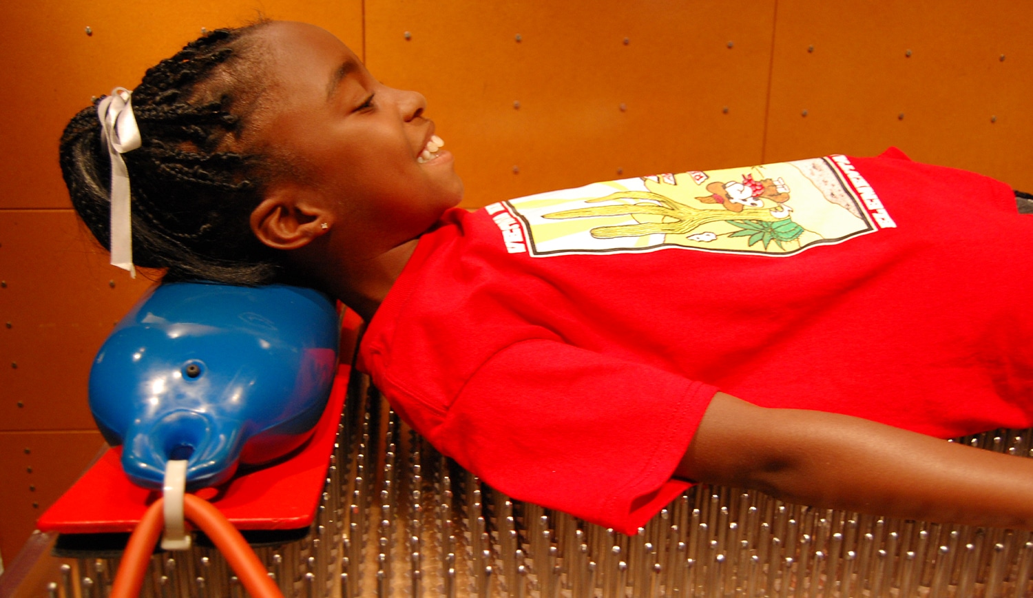 Child smiling on bed of nails at children's science center, an interactive exhibit demonstrating physics of pressure