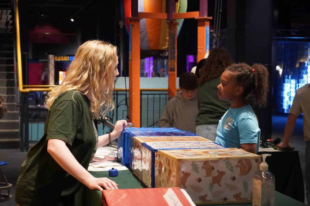 An educator talks with a child at a table surrounded by interactive displays.