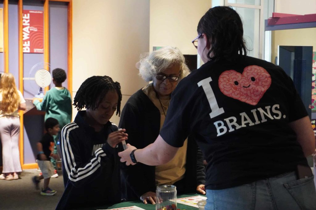 An educator assists a child and an adult during a hands-on science activity at a table.